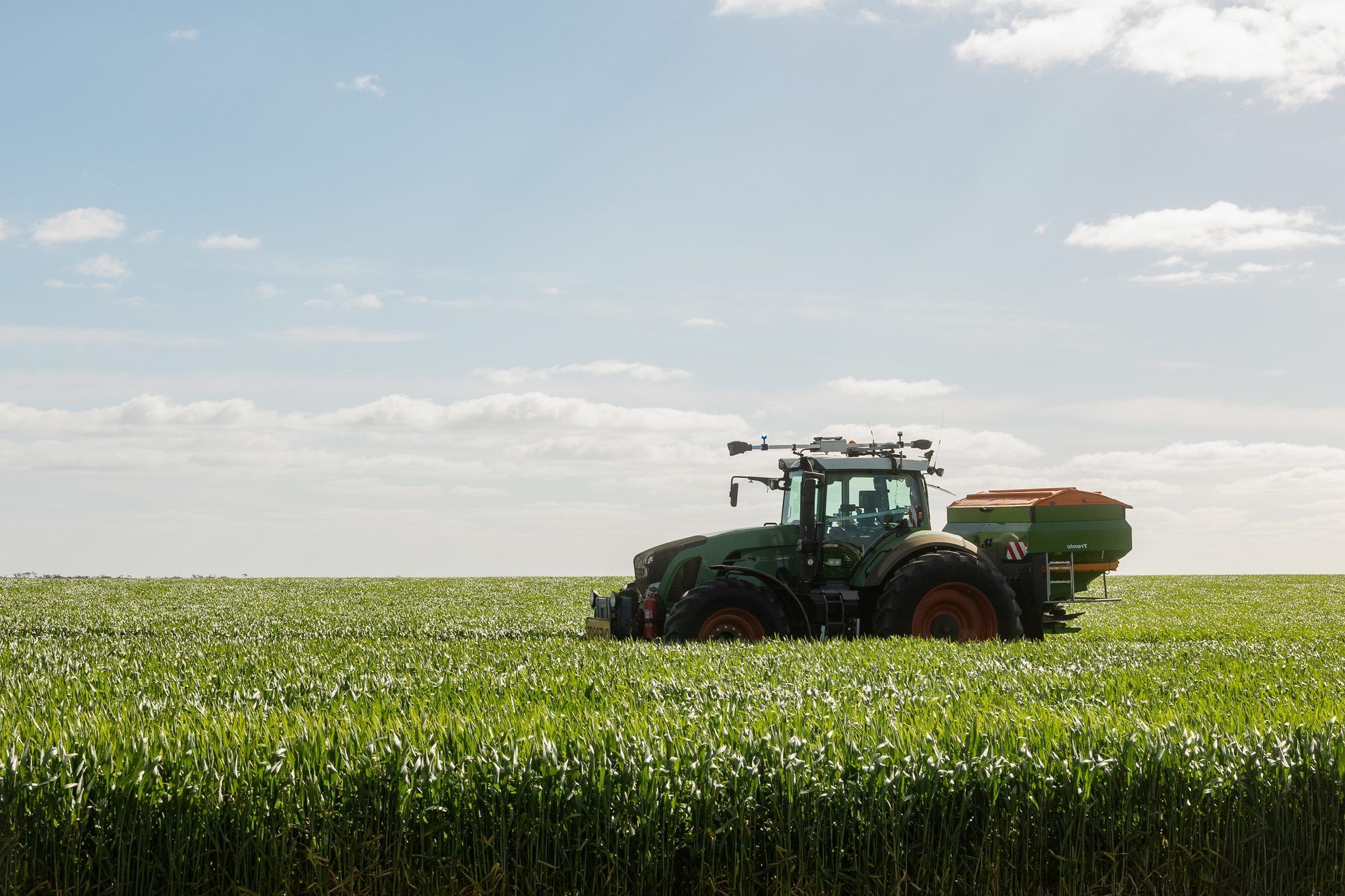 Ornata-equipped Fendt tractor and spreader in a green wheat crop