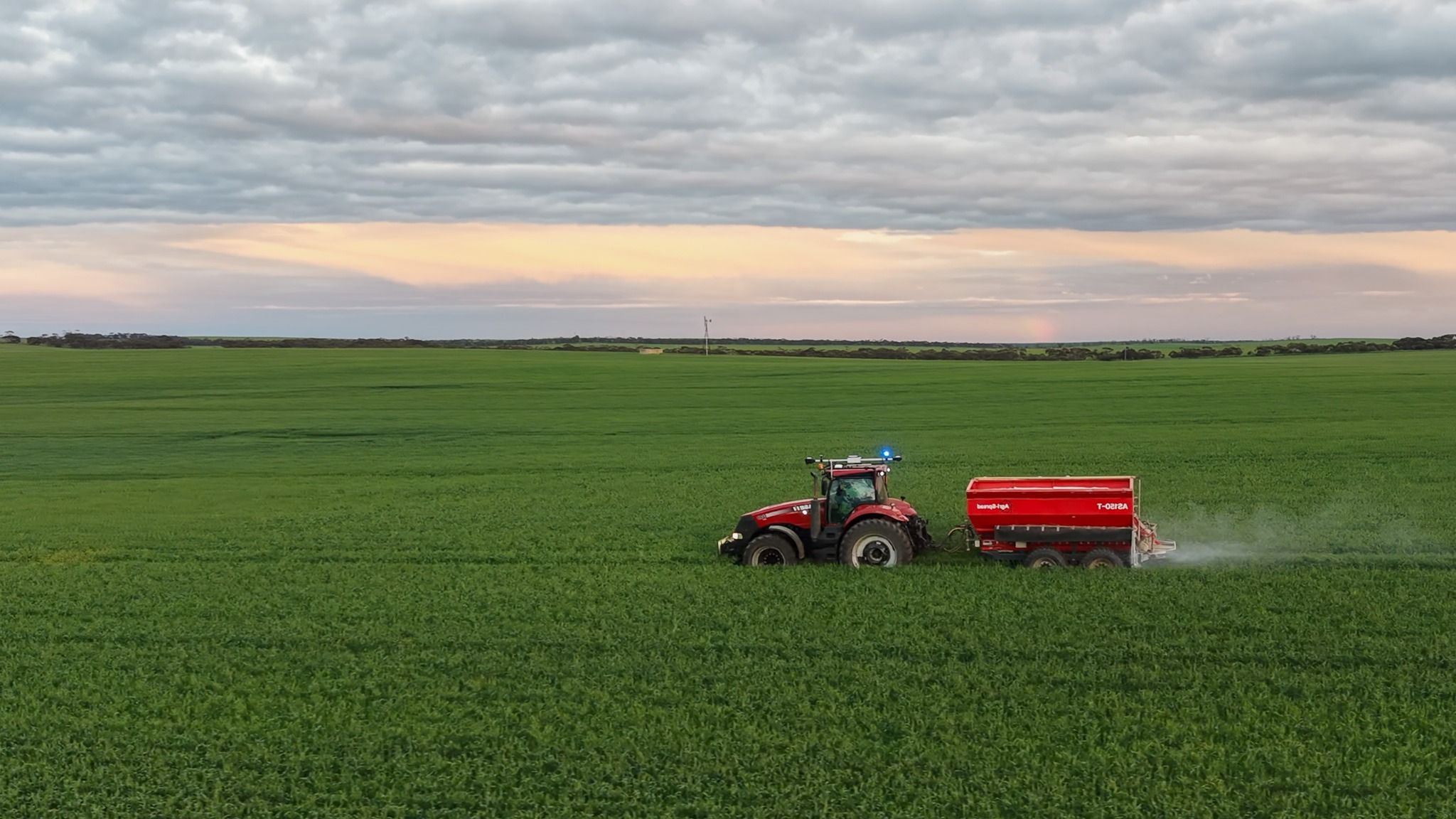 Ornata-equipped tractor and spreader working a green wheat paddock at dusk