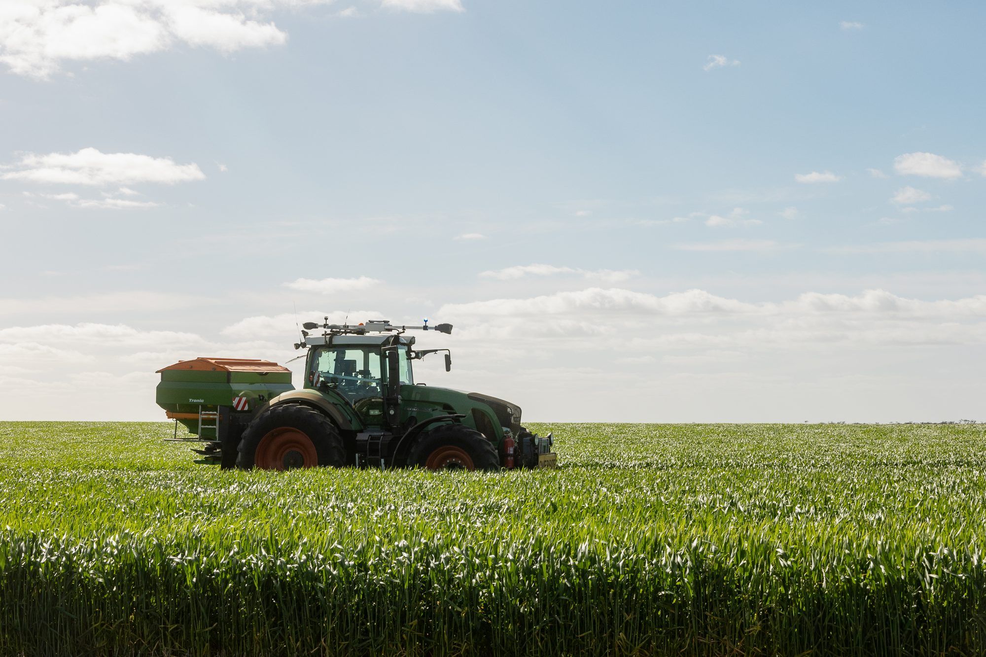 Ornata-equipped tractor spreading fertiliser across a green wheat crop